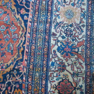 Detailed view of a woven rug featuring elaborate floral designs in rust, navy, cream, and pink tones.