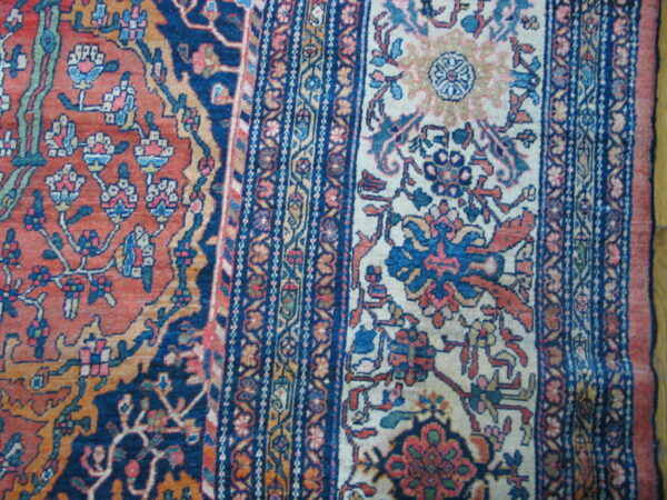 Detailed view of a woven rug featuring elaborate floral designs in rust, navy, cream, and pink tones.