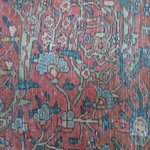 Detailed close-up of a distressed floral rug in rust, olive green, and dark blue.