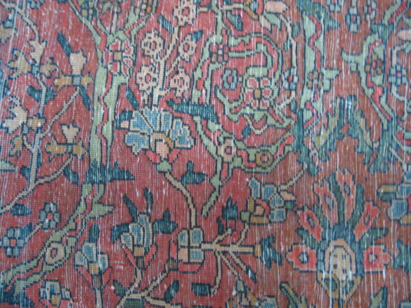 Detailed close-up of a distressed floral rug in rust, olive green, and dark blue.