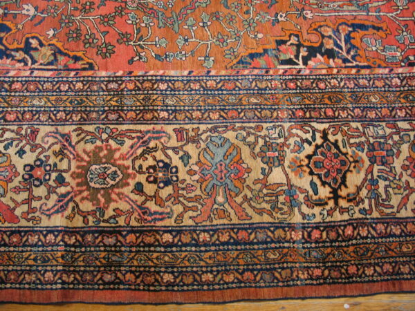 Ornate floral rug pattern in rust, tan, and navy blue with detailed borders shown on a wood floor.