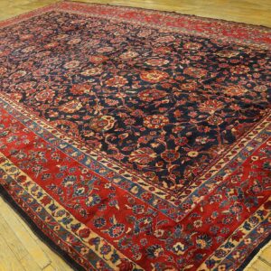 Low-pile rug with a dark blue floral field and wide red border rests on light colored wooden plank flooring.
