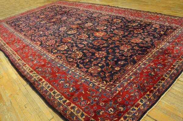 Low-pile rug with a dark blue floral field and wide red border rests on light colored wooden plank flooring.