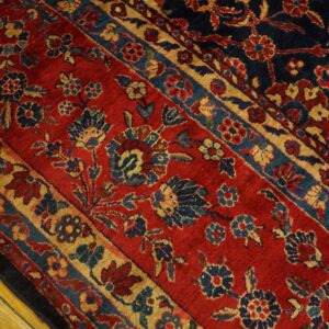 Red rug with dense blue and gold floral patterns separated by borders, resting on wood planks.