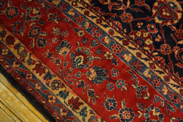 Red rug with dense blue and gold floral patterns separated by borders, resting on wood planks.