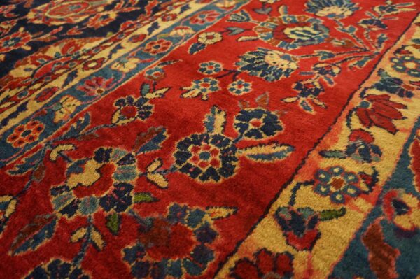 A rug surface detail in red, navy blue, and gold, featuring intricate borders and floral designs.