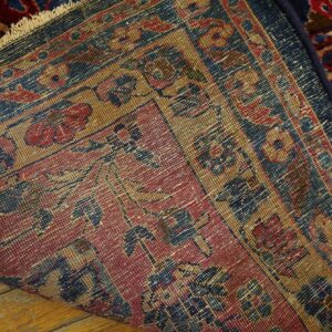 The detailed red, tan, and blue backing of a patterned rug is visible over worn wooden floors.