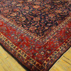 Navy floral rug with a wide red border rests on bright yellow distressed hardwood planks.