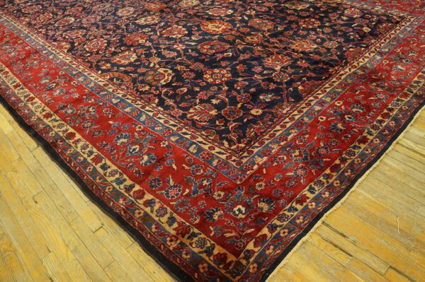 Navy floral rug with a wide red border rests on bright yellow distressed hardwood planks.