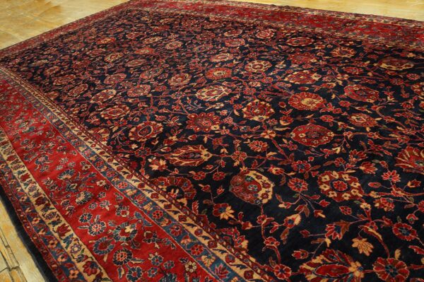 Traditional dark blue rug with dense red and gold floral patterns and a wide red border on wood flooring.