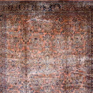 Ornate traditional rug with a salmon field and dense floral patterns in navy blue and gold.