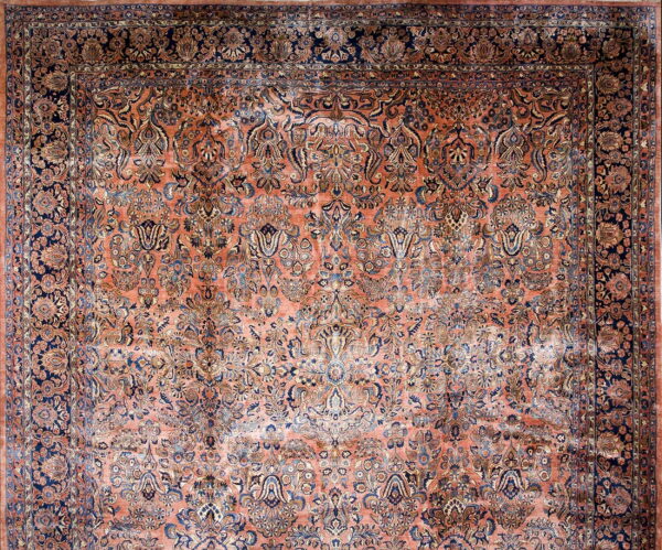 Ornate traditional rug with a salmon field and dense floral patterns in navy blue and gold.