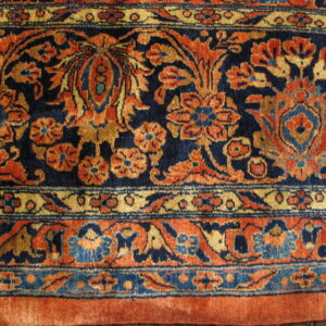 Close-up of a short pile rug with traditional floral patterns in navy, burnt orange, gold, and light blue.
