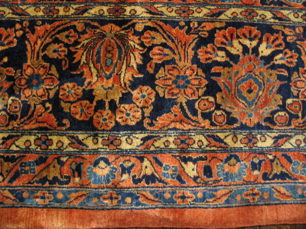 Close-up of a short pile rug with traditional floral patterns in navy, burnt orange, gold, and light blue.