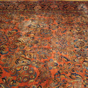 Low-pile rust rug featuring a dense traditional floral pattern in navy, gold, and light blue accents.