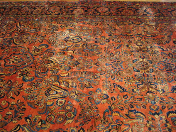 Low-pile rust rug featuring a dense traditional floral pattern in navy, gold, and light blue accents.