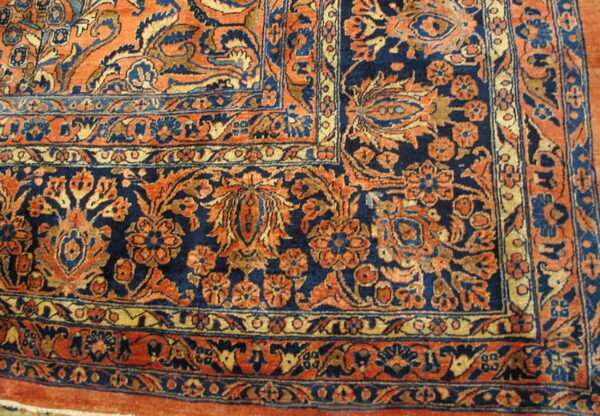 Intricate close-up of a rug corner showing floral and vine patterns in navy blue, terracotta, and gold.