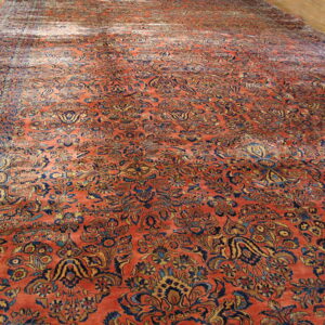 Large, low-pile rug featuring a dense floral pattern in deep orange, navy, and gold on a light hardwood floor.