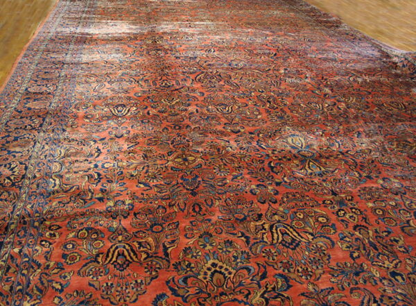 Large, low-pile rug featuring a dense floral pattern in deep orange, navy, and gold on a light hardwood floor.