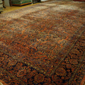 A large orange and navy rug displaying a dense traditional pattern is laid on a hardwood floor.