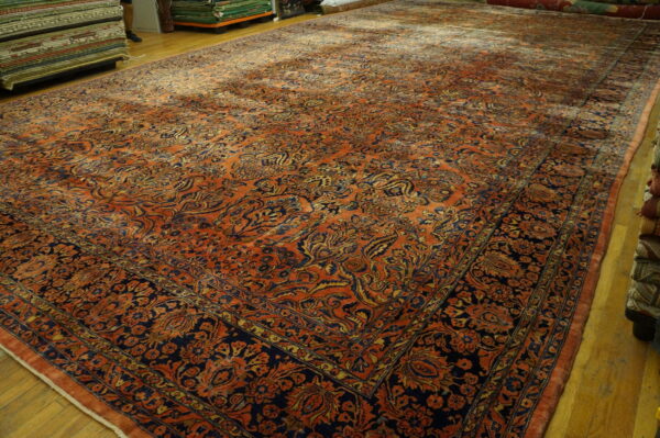A large orange and navy rug displaying a dense traditional pattern is laid on a hardwood floor.
