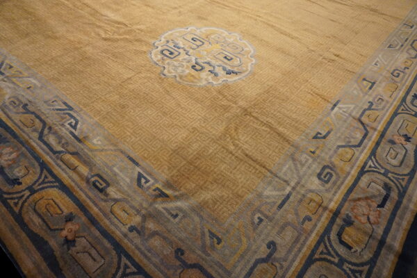 Gold rug with subtle geometric texture, a central blue medallion, and a wide multicolored border.