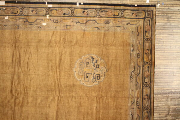 Wrinkled ochre rug with detailed black borders and a central motif rests on light wood floors.