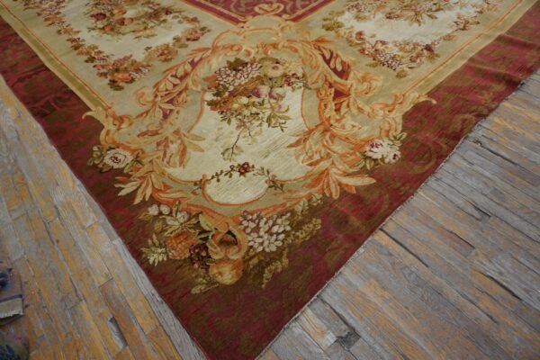 Low-pile rug with ornate cream and gold floral motifs bordering a wide burgundy field on wood floors.
