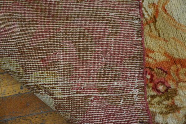 The beige and orange pile rug is folded, exposing the striped maroon and brown backing on wood planks.