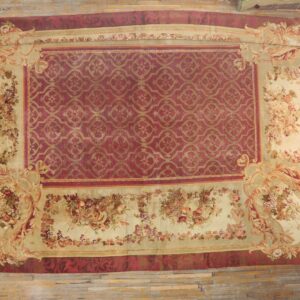 Large red rug featuring a gold geometric center and extensive beige floral fruit motif borders on wood floor.
