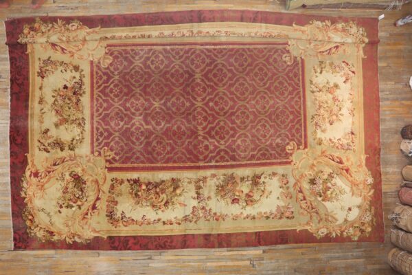 Large red rug featuring a gold geometric center and extensive beige floral fruit motif borders on wood floor.