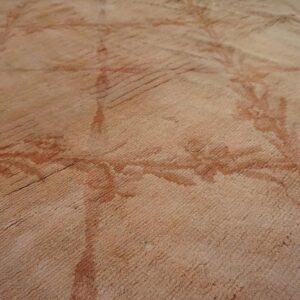 A close-up view of a pink rug showing ribbed texture and a faded floral pattern in darker reddish hues.