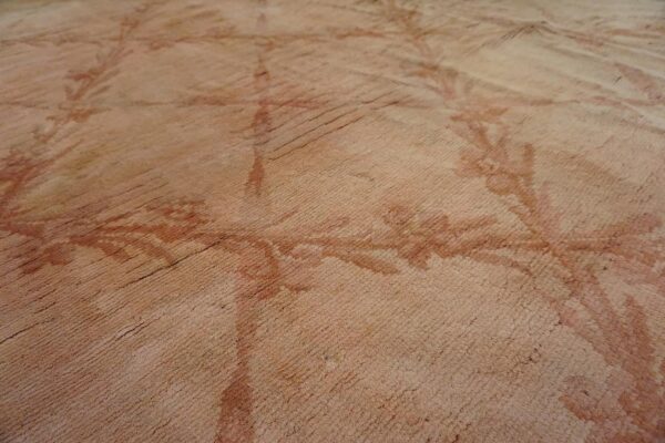 A close-up view of a pink rug showing ribbed texture and a faded floral pattern in darker reddish hues.