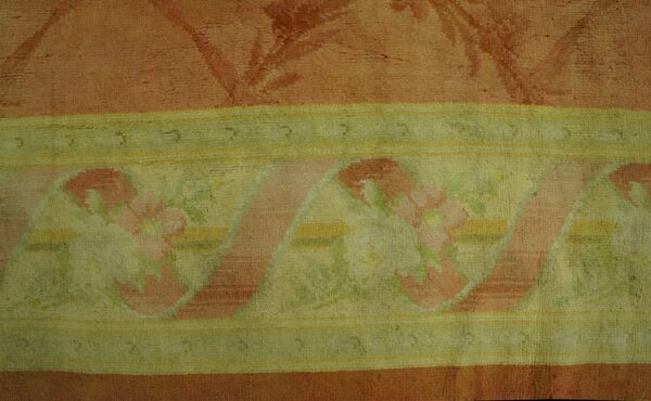 Muted coral rug features a wide border with pink floral patterns, pale green background, and yellow stripes.