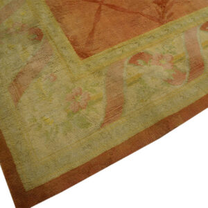 Detail shot of a rust rug with a wide sage border containing stylized pink floral patterns.