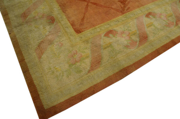 Detail shot of a rust rug with a wide sage border containing stylized pink floral patterns.