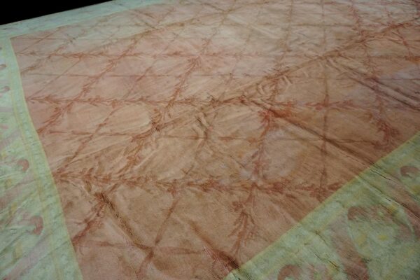 Wrinkled, low-pile rug with a blush field, reddish trellis pattern, and faded pale green border.