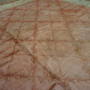 Faded beige rug with a reddish trellis pattern and green border visible against a wooden floor.