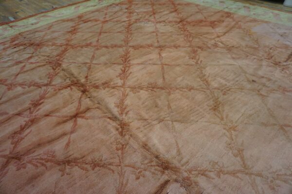Faded beige rug with a reddish trellis pattern and green border visible against a wooden floor.