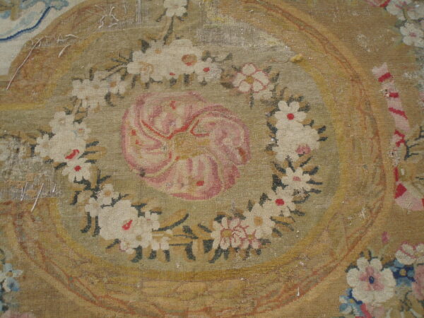 Distressed flatweave rug featuring a large faded pink rosette surrounded by a detailed white and green floral garland.