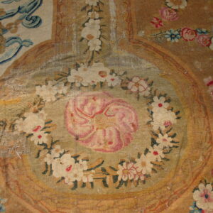 Faded flatwoven rug detail shows a central pink flower medallion surrounded by white floral garlands on a tan field.