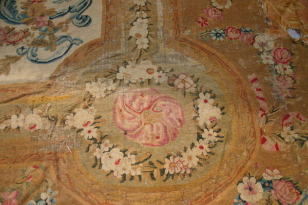 Faded flatwoven rug detail shows a central pink flower medallion surrounded by white floral garlands on a tan field.