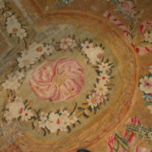 Flatweave rug with a central pink medallion and floral spray on a faded tan and gold background.