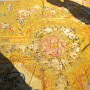 Worn yellow textile fragment with pink and white floral designs, visible damage, and large dark shadows.