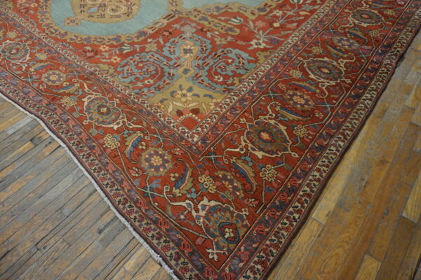 Red, blue, and gold traditional patterned rug corner showing floral motifs on rustic wood floor.