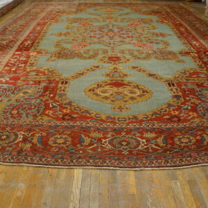 Large rug with detailed rust red borders and light blue center medallion on rustic wood flooring.
