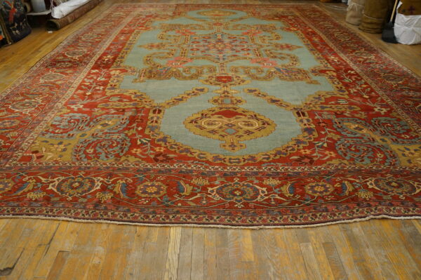 Large rug with detailed rust red borders and light blue center medallion on rustic wood flooring.