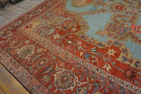 Close-up of a floral patterned rug in rich red, pale blue, and tan on rustic wooden flooring.