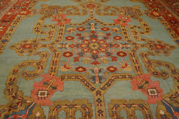Ornate floral rug featuring a soft blue-green field accented by red, gold, and coral traditional motifs.