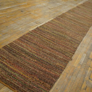 Textured, multicolored brown runner rug with thin bright stripes rests upon a worn hardwood floor.